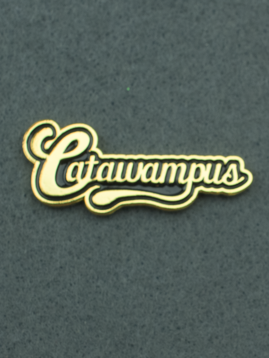 An enamel pin that says "Catawampus" in gold. on a black background.