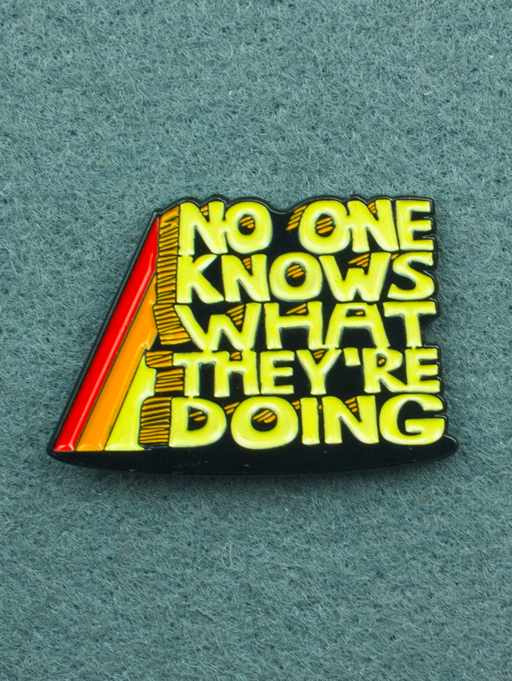 An enamel pin that reads "no One Knows What They're Doing" in yellow text with a school house rock aesthetic. 