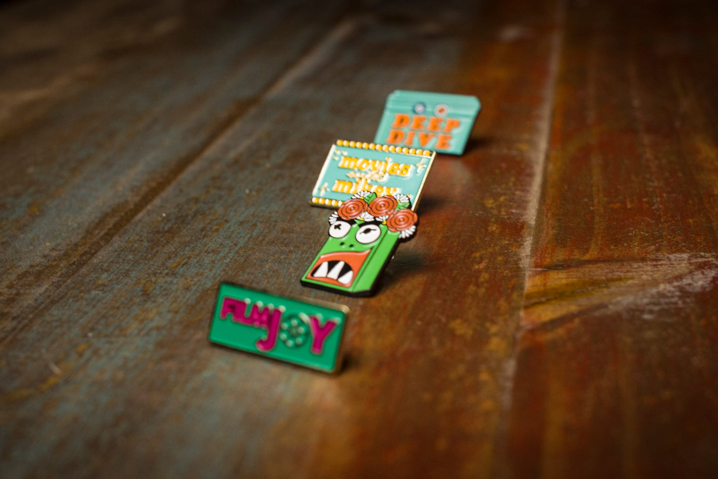 Four Filmjoy enamel pins on a wooden table